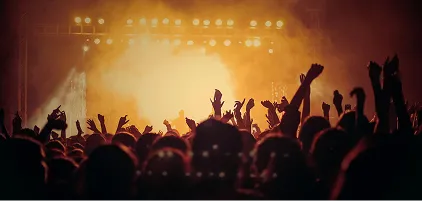 A silhouetted crowd with hands raised against warm stage lighting